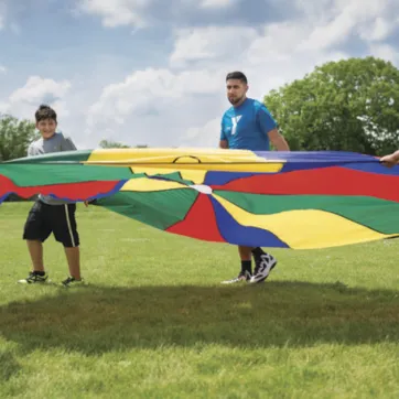 Youth playing in field with rainbow parachute